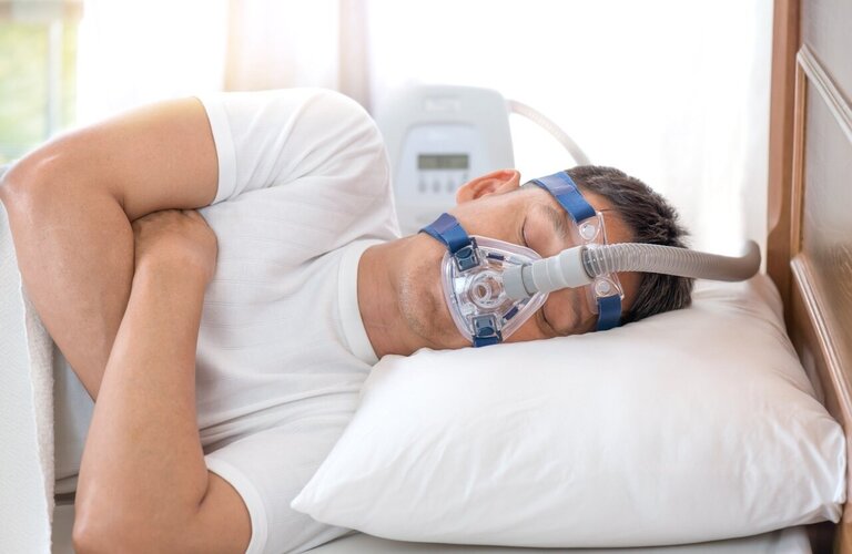 Junger Mann liegt schlafend im Bett und trägt eine Nasenmaske 